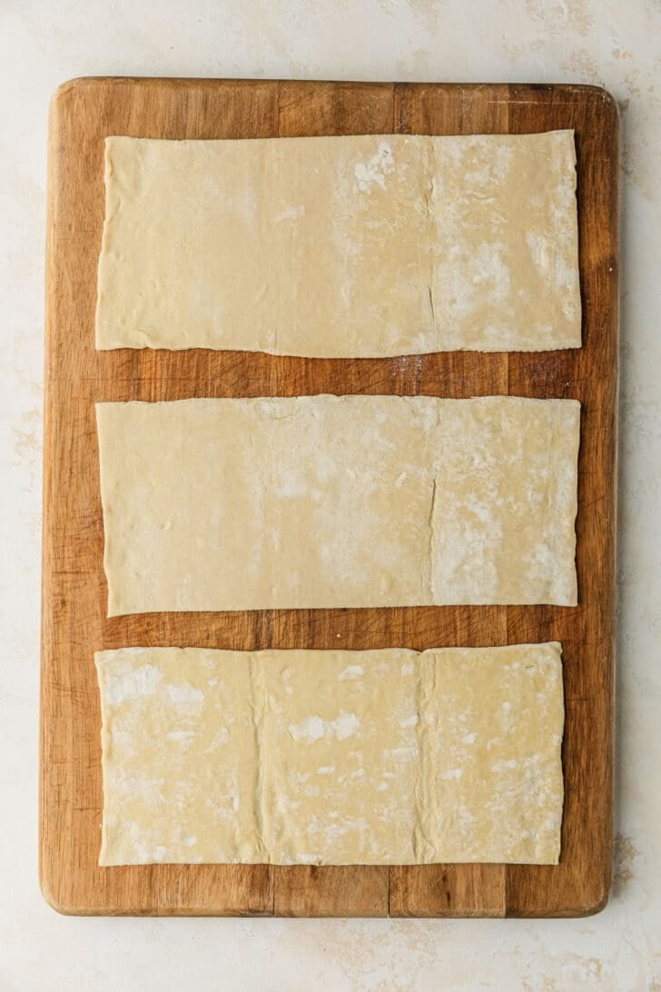 A wood board with puff pastry on a tan counter.