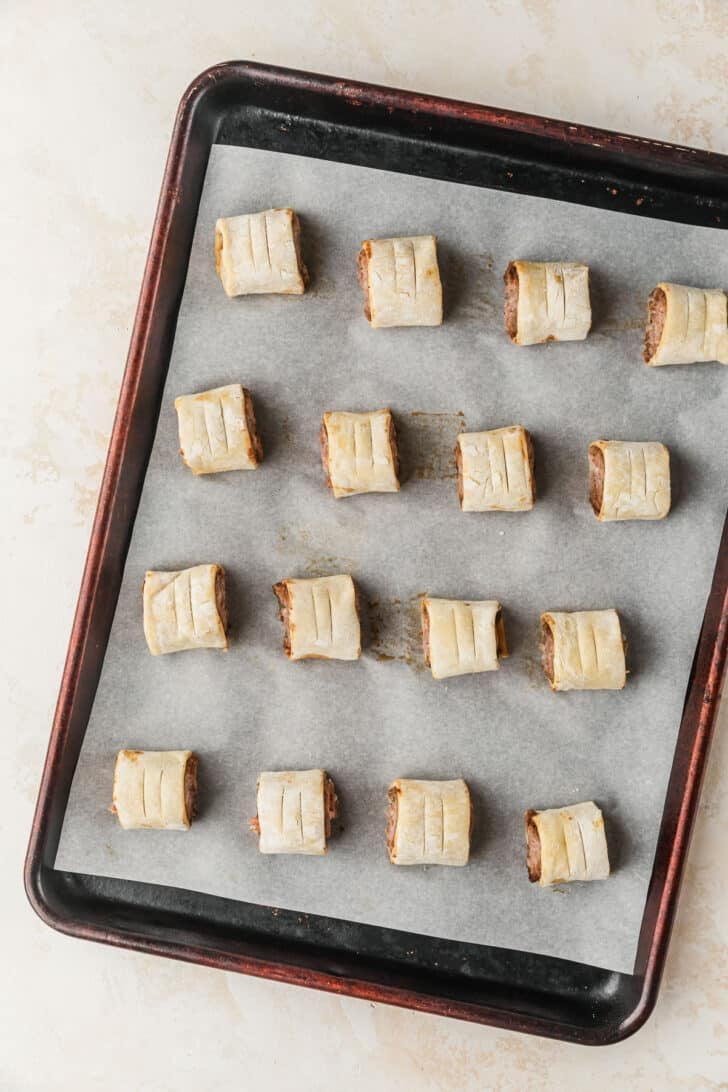A sheet pan of raw pork and apple sausage rolls on a tan counter.