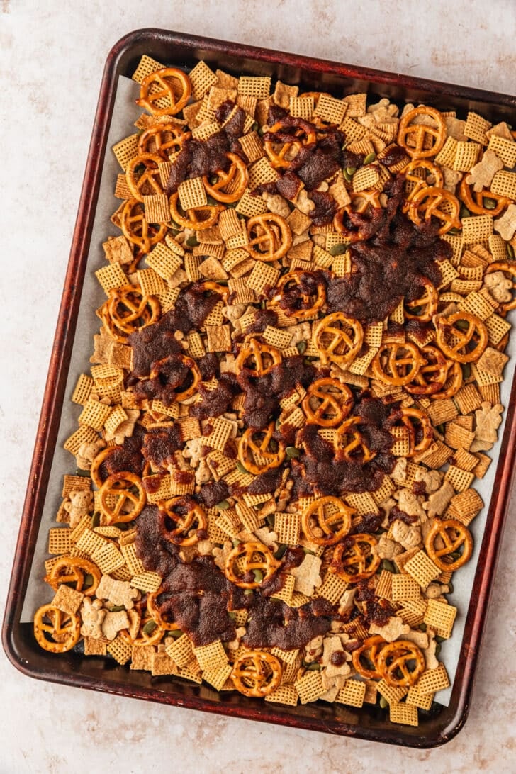 A pan of pumpkin spice autumn snack mix topped with brown sugar-butter mix on a tan counter.