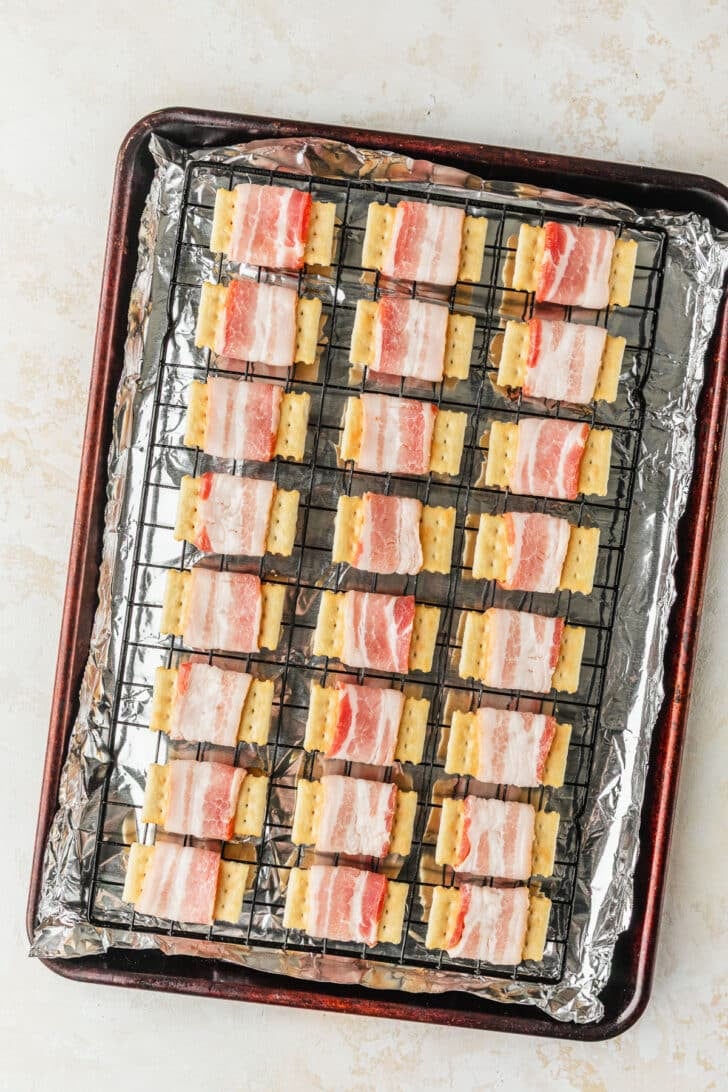 Club crackers wrapped in meat on top on a wire rack with a tan background.