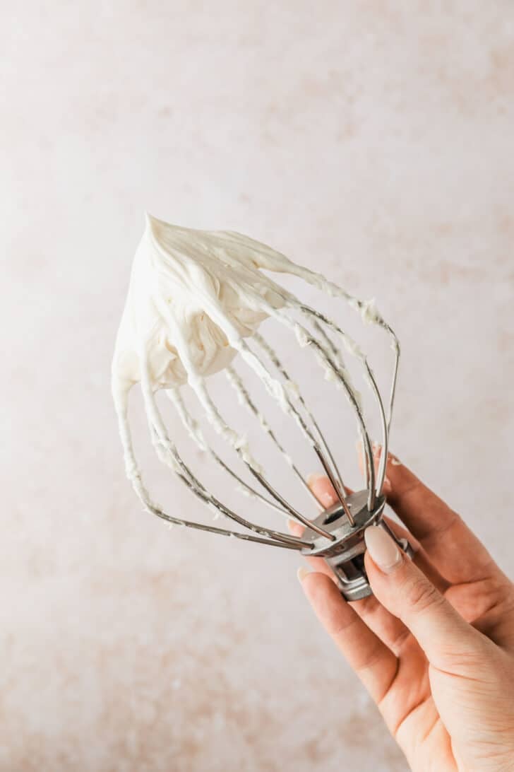 A hand holding a whisk of cream cheese frosting for pumpkin mini bundt cakes.