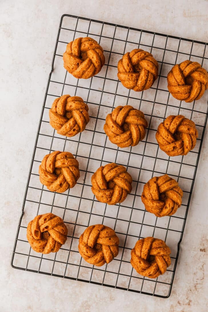 A wire rack of pumpkin mini bundt cakes on a beige marble counter.