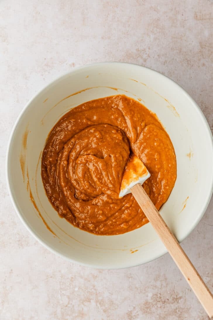 A white bowl of pumpkin cake batter on a tan table.