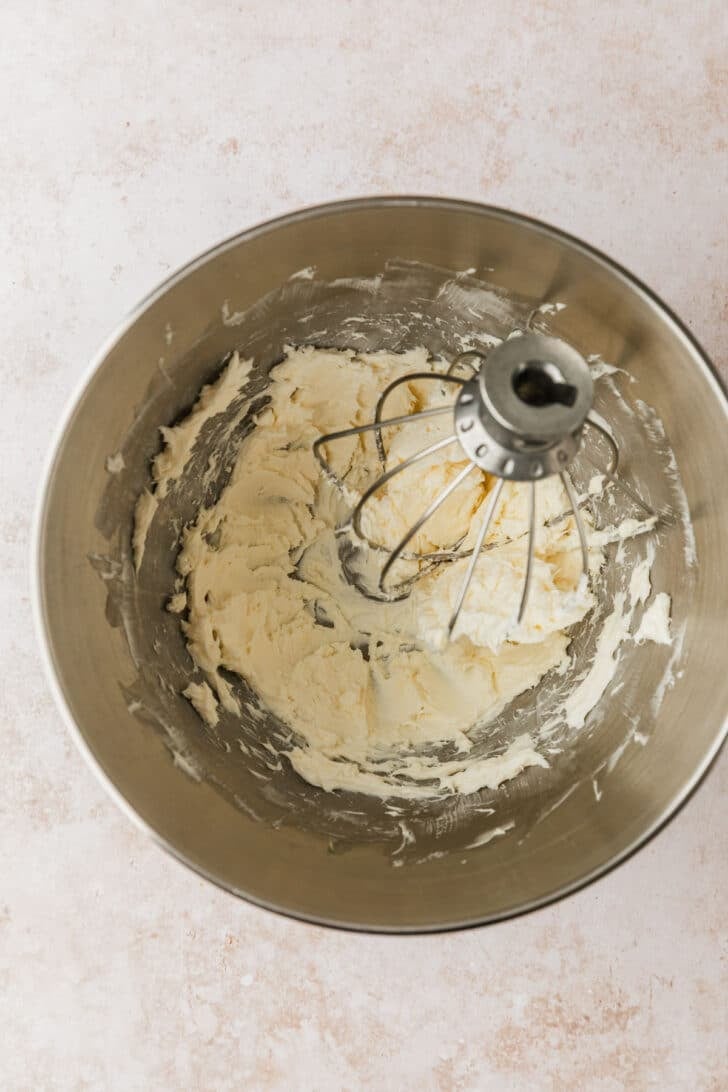 A silver bowl of whipped butter and cream cheese on a beige table.