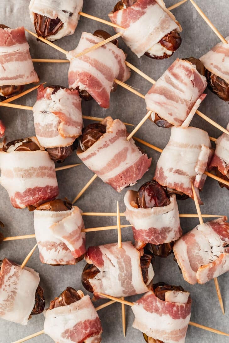 Raw bacon wrapped dates on parchment paper.