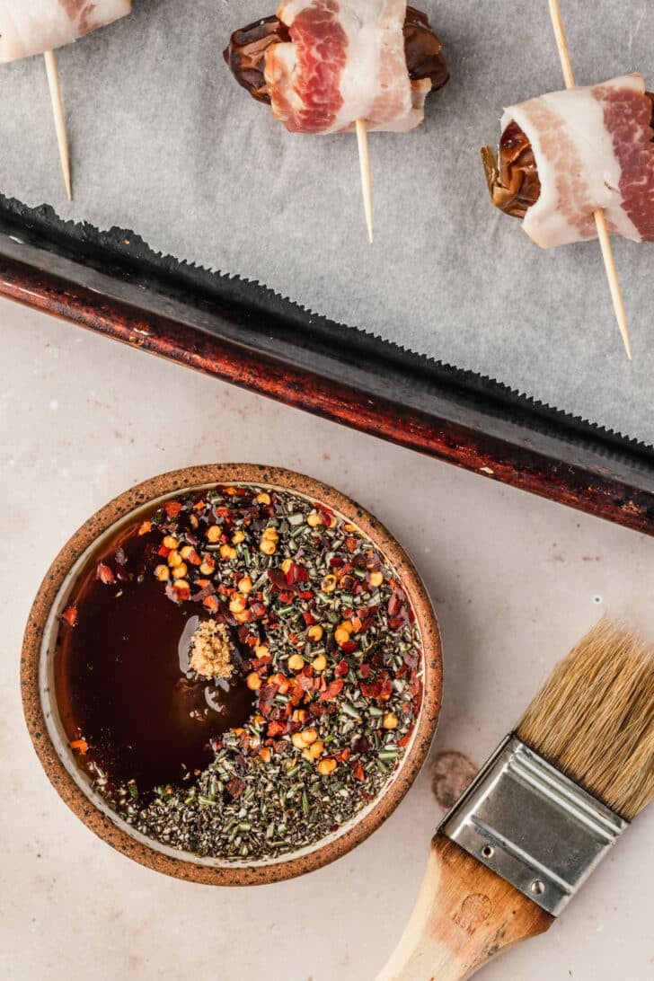 A brown bowl of syrup, brown sugar, and spices next to a sheet pan with a tan background.
