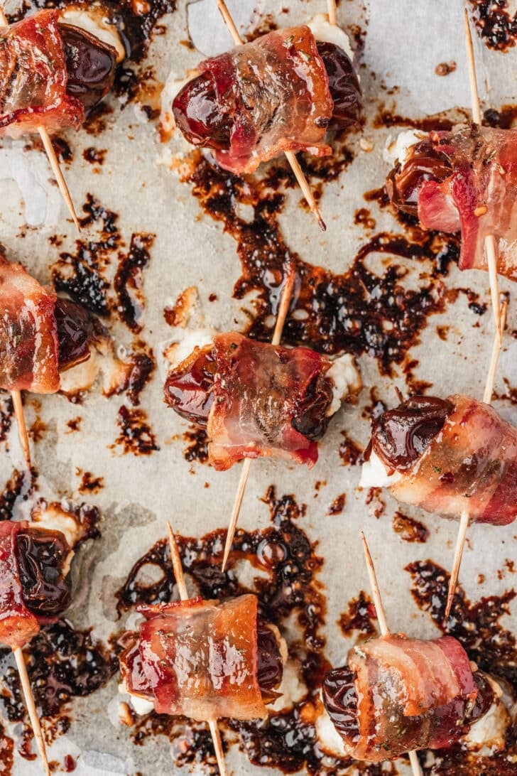 Maple glazed bacon wrapped dates stuffed with goat cheese on parchment paper.