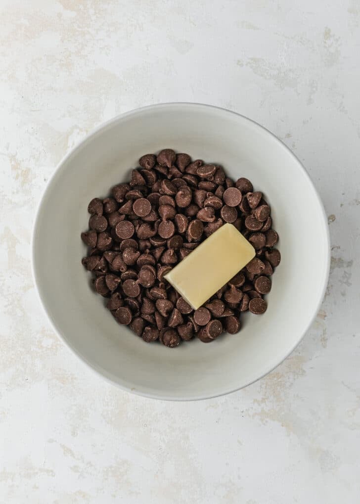 A white bowl of chocolate chips and butter on a tan counter.