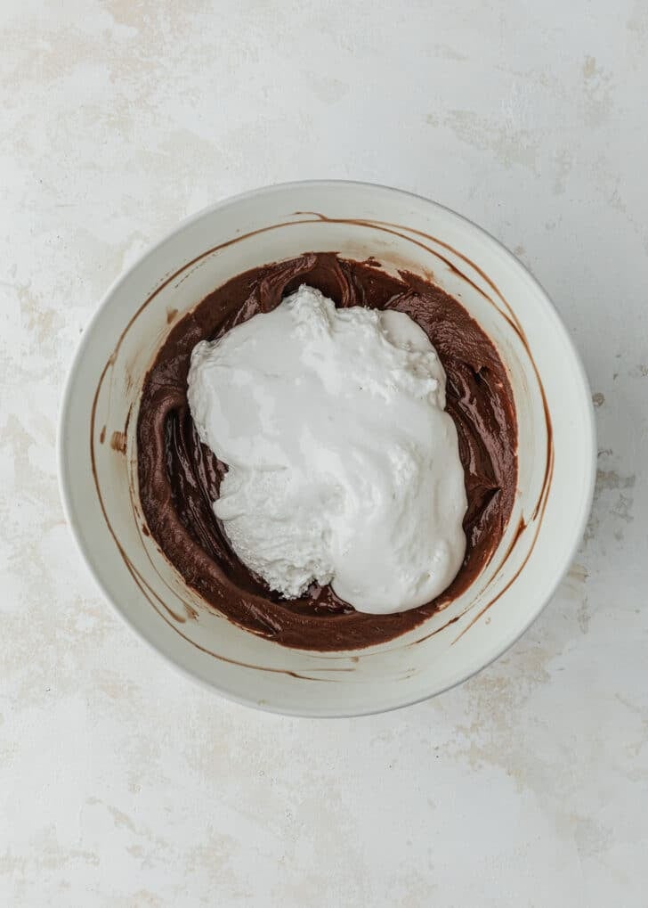 A white bowl of melted chocolate and marshmallow fluff on a beige table.