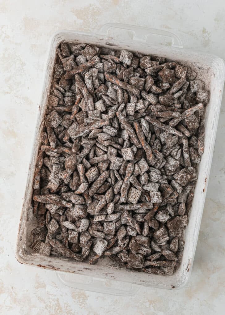 A container of hot cocoa Christmas puppy chow on a tan table.
