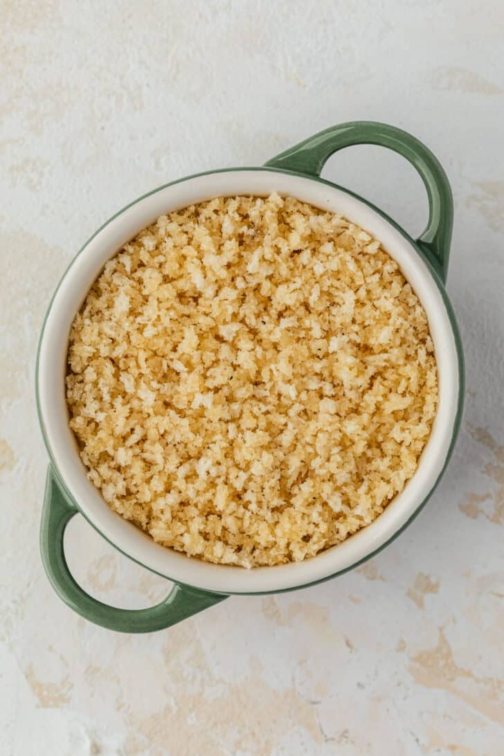 A green ramekin of cheese and bread crumbs on a tan table.