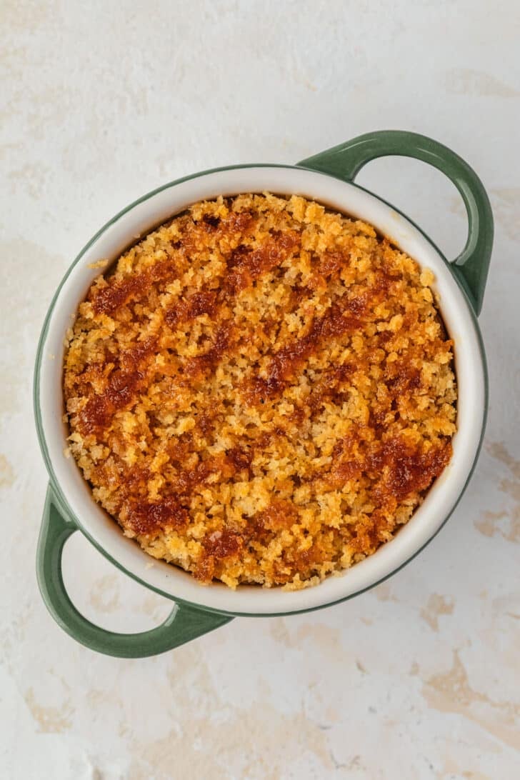 A green ramekin of baked boursin cheese with hot honey on a tan counter.