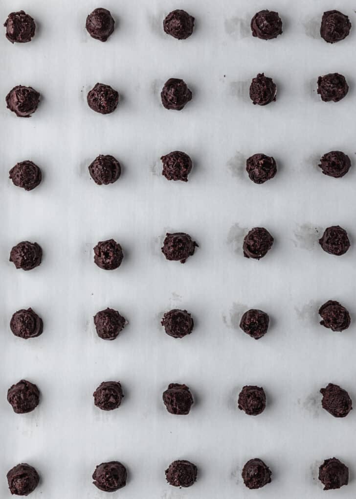 Raw mini chocolate brownie crinkle cookies on parchment paper.