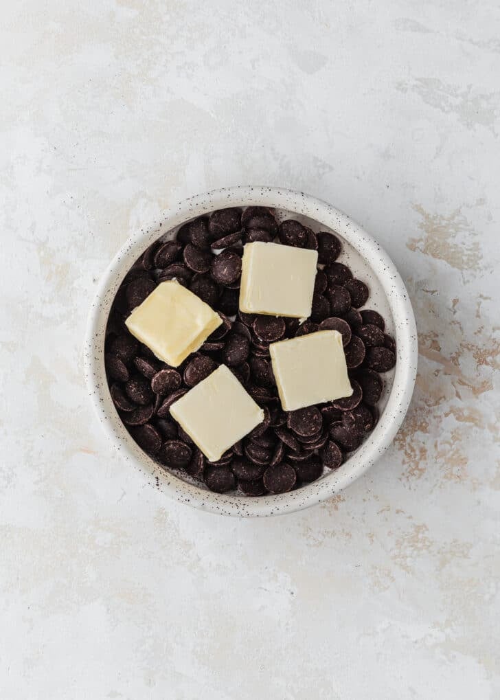A white bowl of chocolate chips and butter on a beige table.