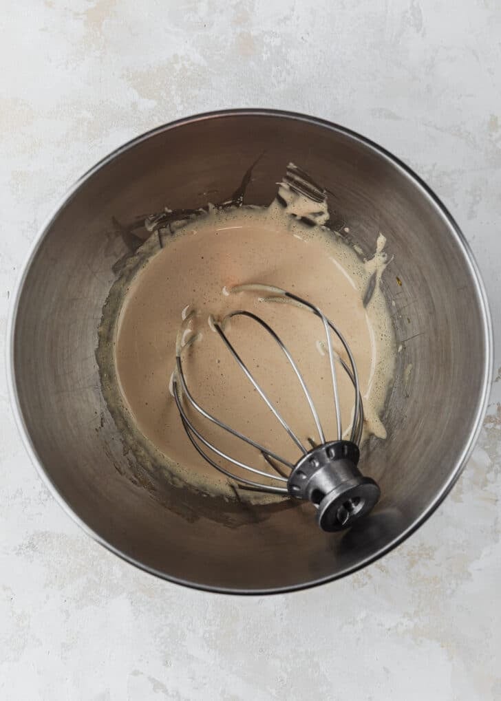 A silver bowl with whipped eggs and sugar on a beige counter.