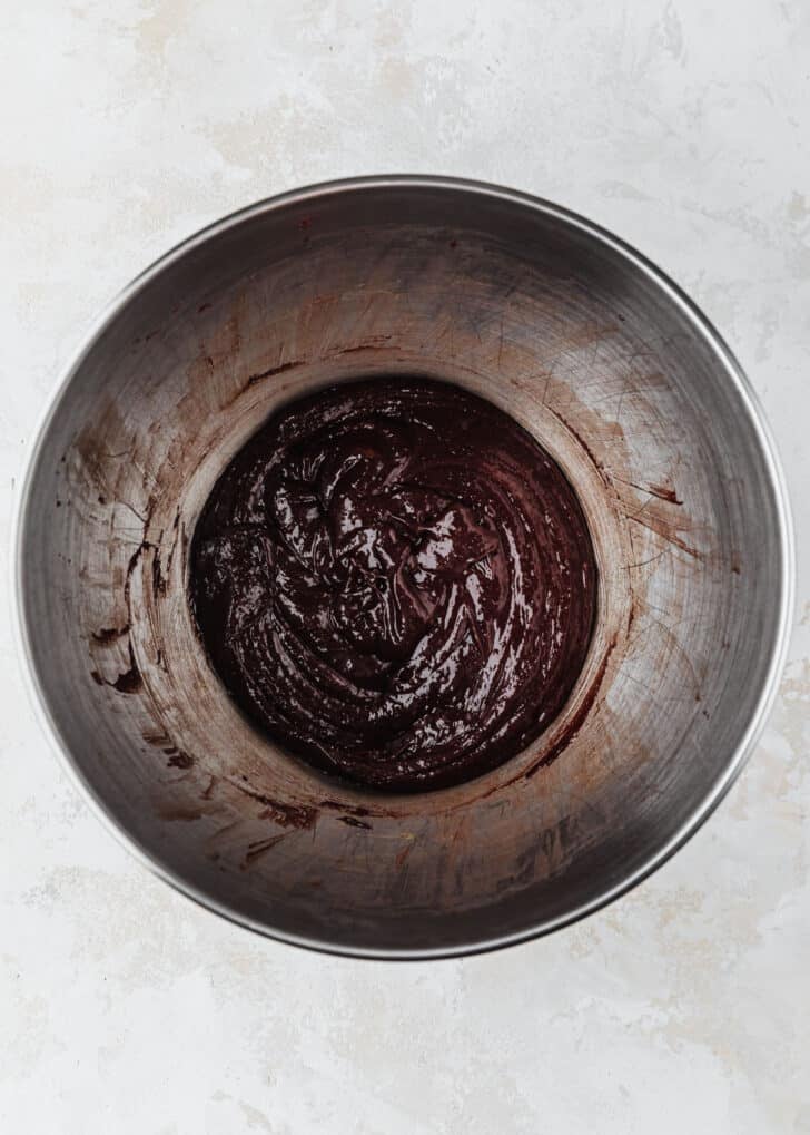 A silver bowl of mixed eggs, sugar, and chocolate on a beige table.