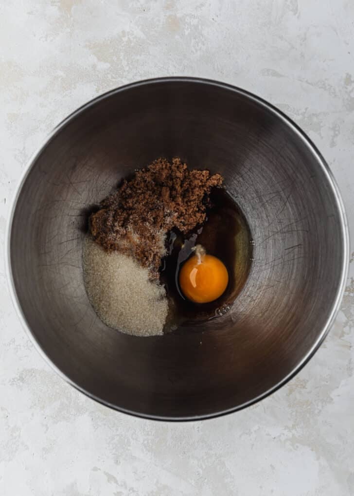 A silver bowl of white sugar, brown sugar, and an egg on a tan counter.