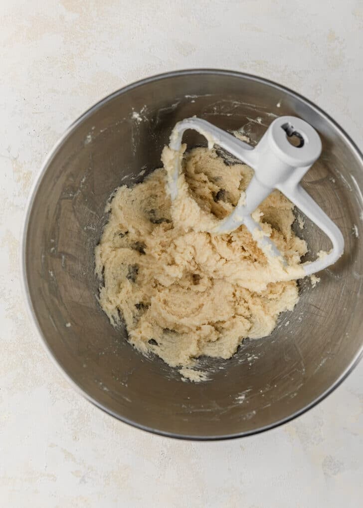 A silver bowl of beaten butter and sugar on a tan table.