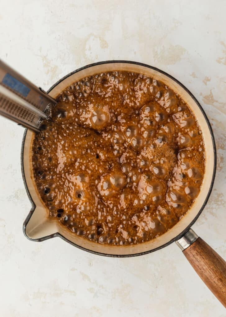 A white pot of bubbling caramel on a tan counter.