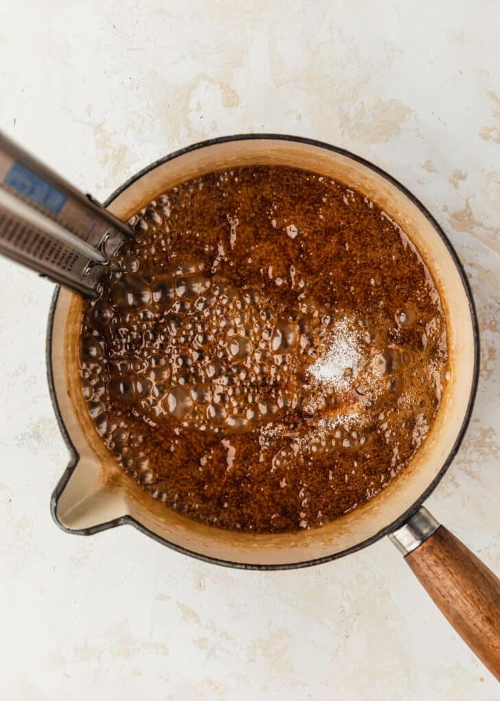 A white pot of toffee sauce with salt and vanilla on a beige table.