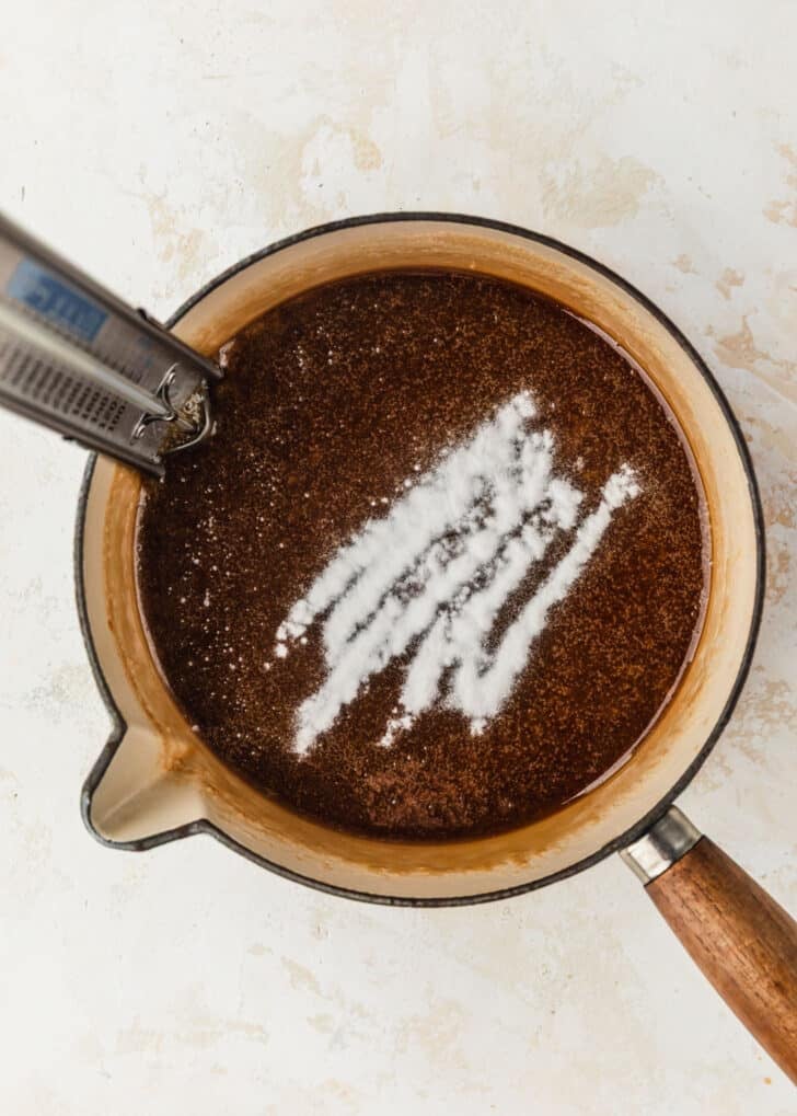 A white pot of caramel with baking soda on a tan counter.