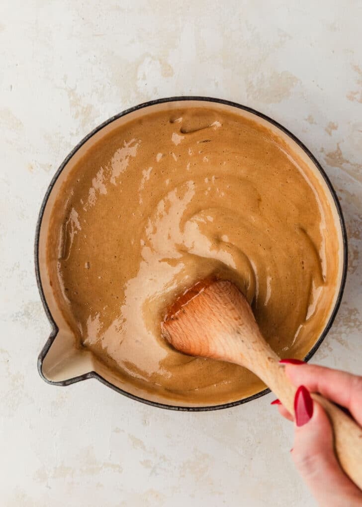 A hand using a spoon to stir toffee sauce in a white pot.