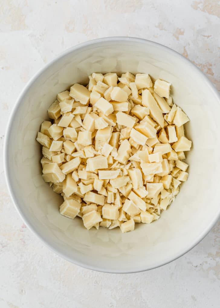 A white bowl of chopped white chocolate on a tan counter.