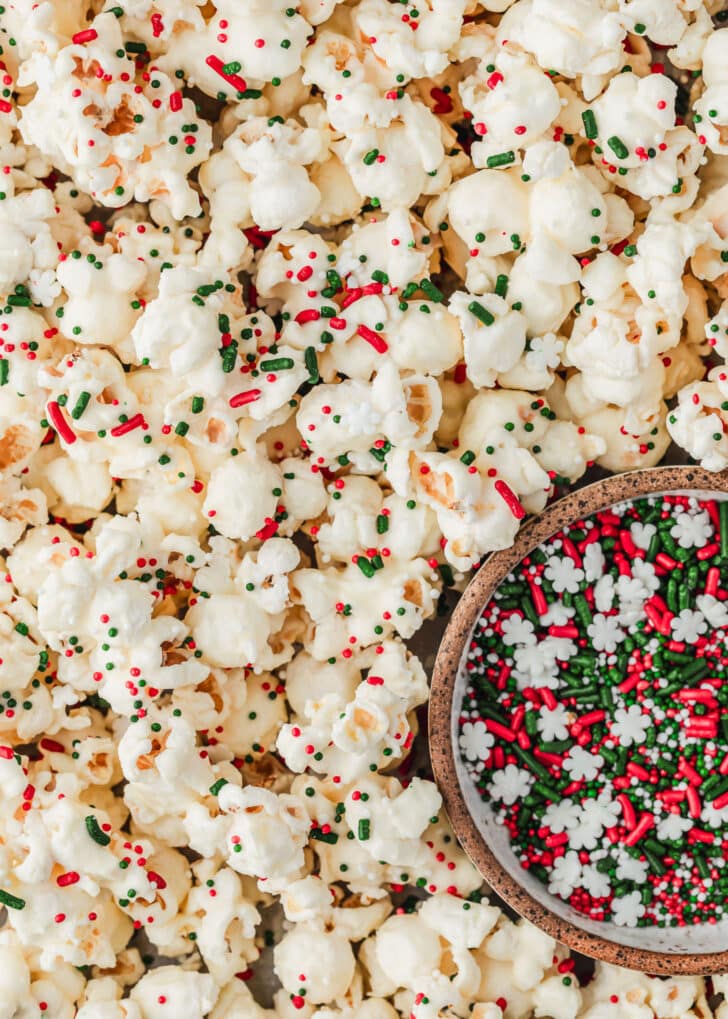 White chocolate popcorn with holiday sprinkles next to a brown bowl of Christmas sprinkles.