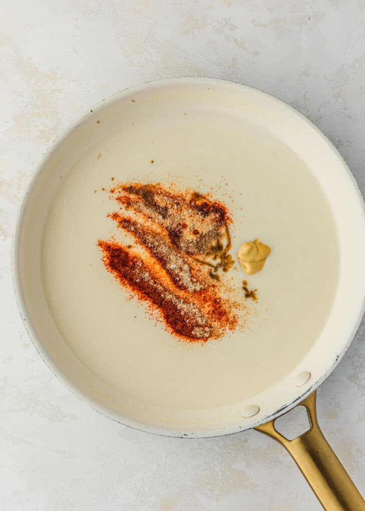 A white pan of bechamel sauce and spices on a white table.
