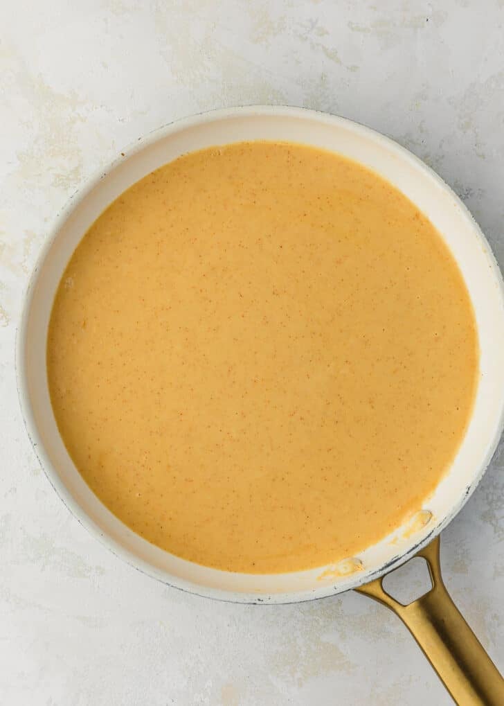 A white pan of beer cheese dipping sauce for pretzels on a white stone counter.