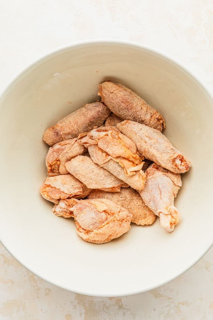 A white bowl of chicken and spices on a beige counter.