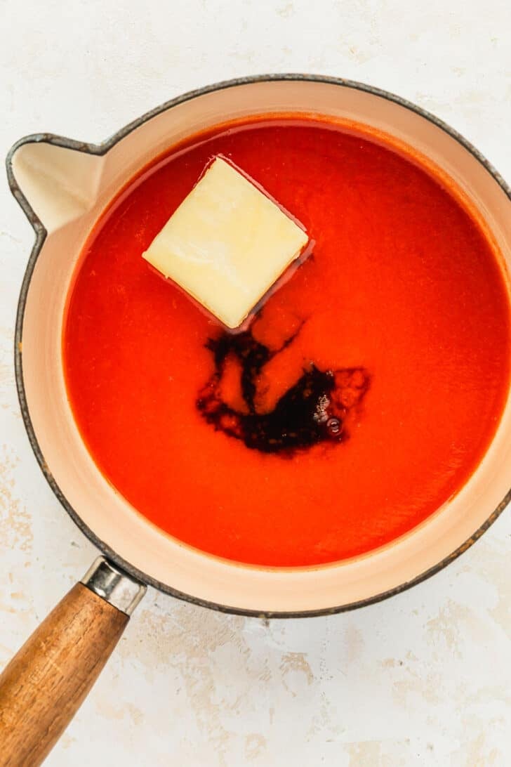 A white pot of hot sauce, butter, and hot honey on a beige counter.