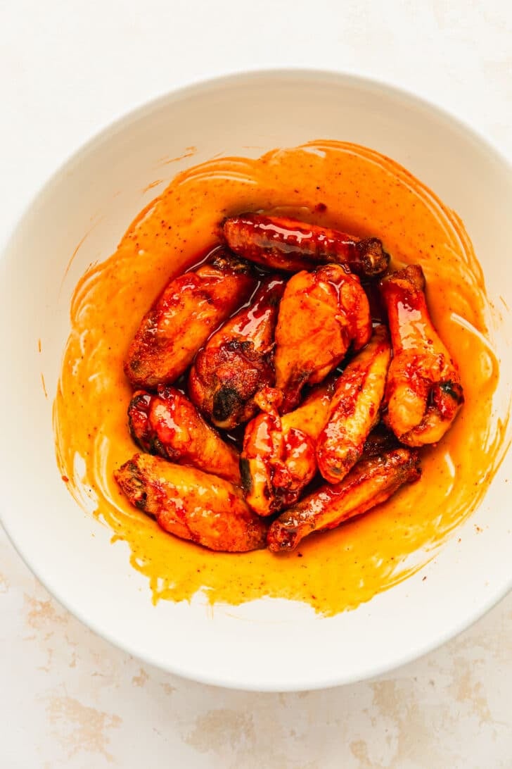 A white bowl of hot honey buffalo wings on a white counter.