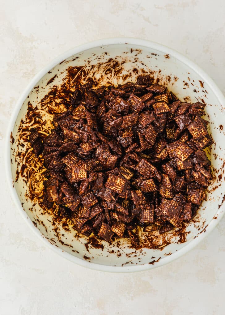 A white bowl of Chex mixed with chocolate on a beige table.