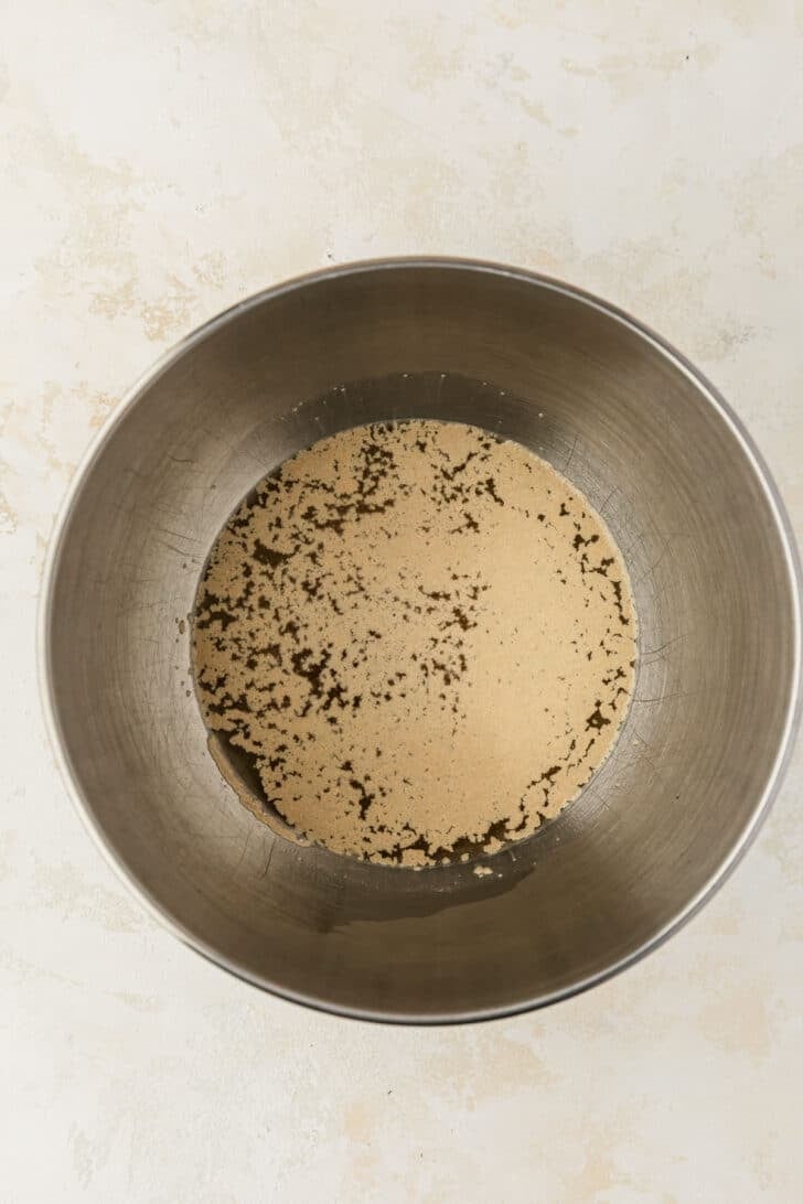A silver bowl of water and yeast on a tan counter.