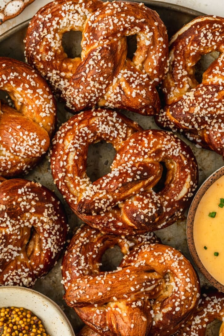 A metal tray of homemade mini soft pretzels next to white bowls of cheese sauce and mustard.