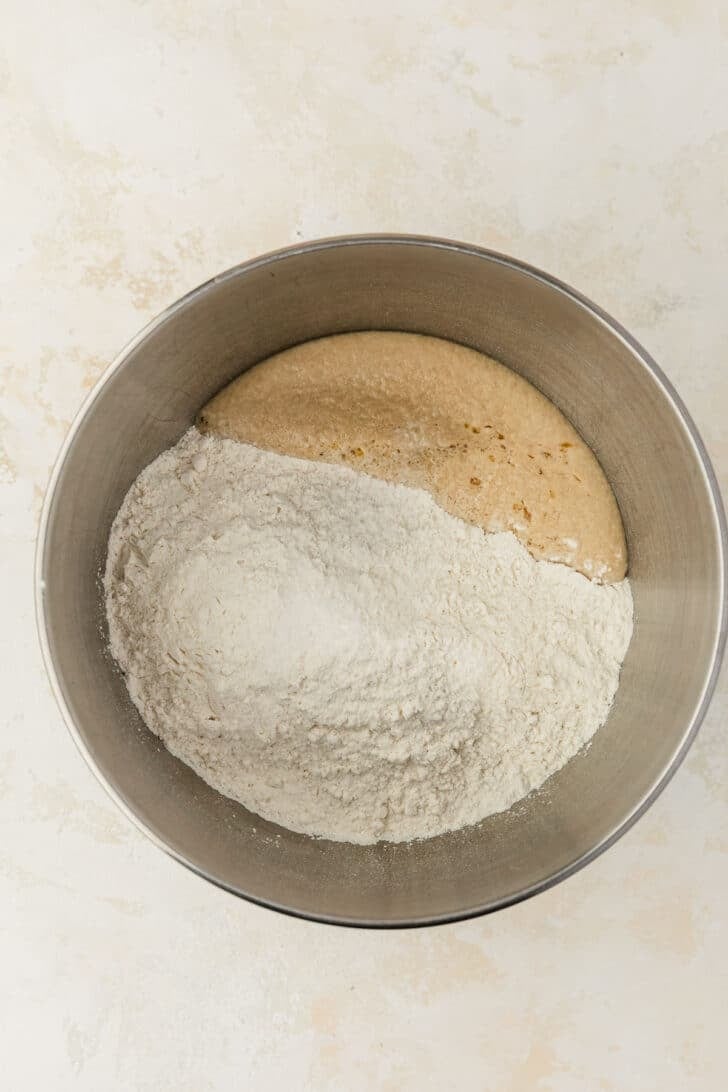 A silver bowl of foamy yeast and flour on a tan counter.