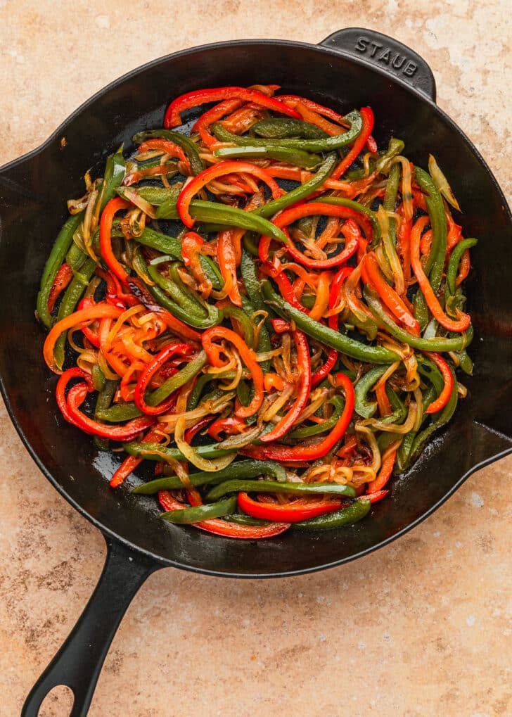 A skillet of sauteed onions and peppers on an orange counter.