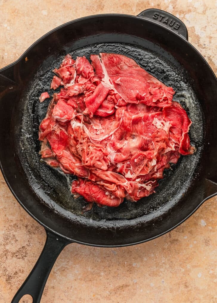A skillet of shaved beef on an orange counter.
