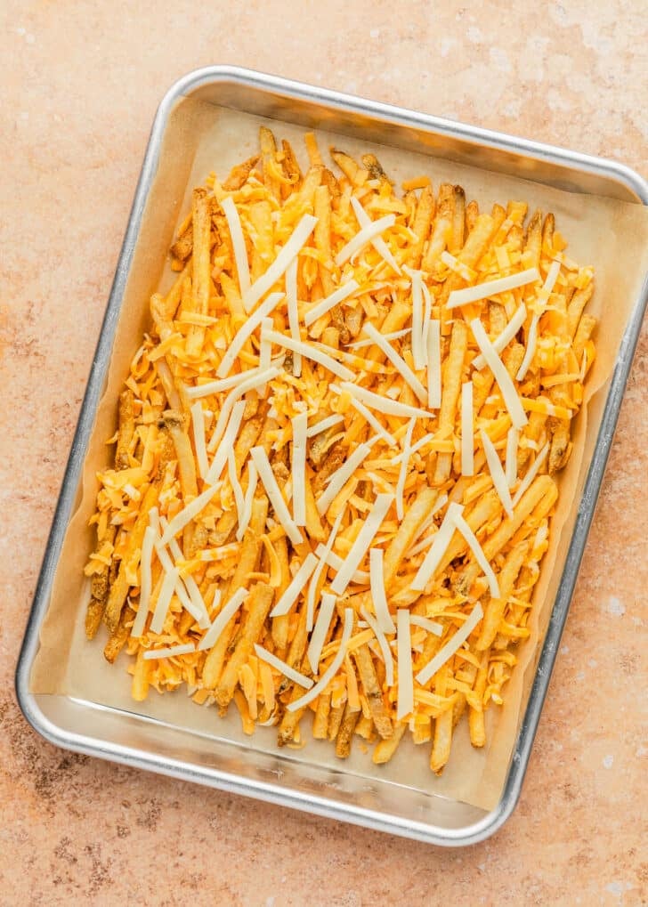 A pan of fries and cheese on a tan counter.