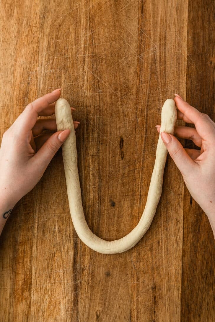 Hands forming dough into a U shape on a wood board.