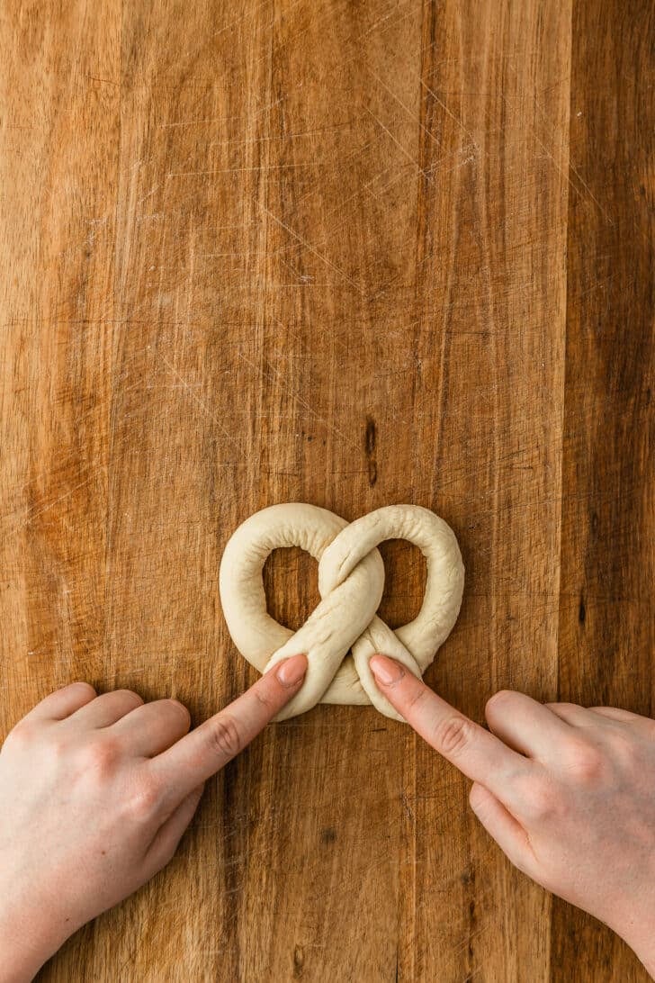 Hands pressing dough for mini soft pretzels on a wood counter.