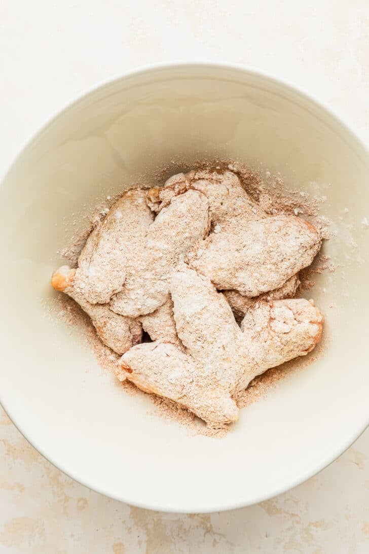 A white bowl of chicken with cornstarch on a white counter.