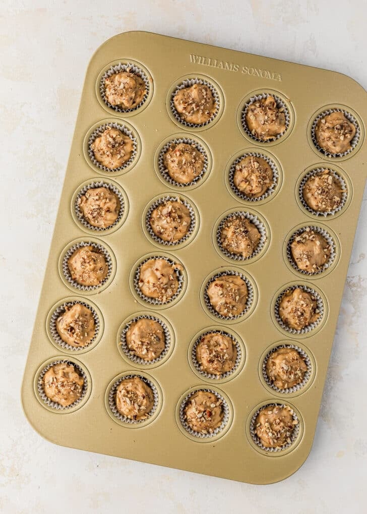 A pan of raw mini banana muffins on a tan table.