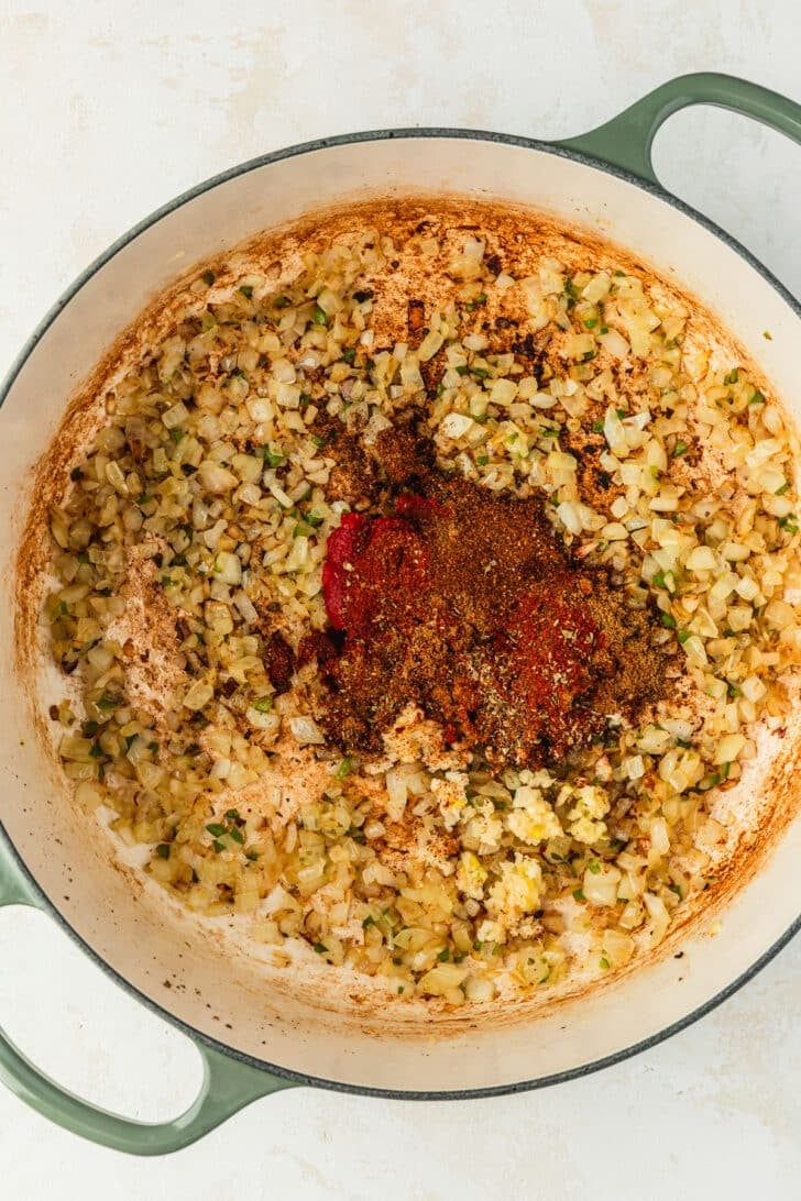 A green Dutch oven of onions, jalapenos, and spices on a tan counter.