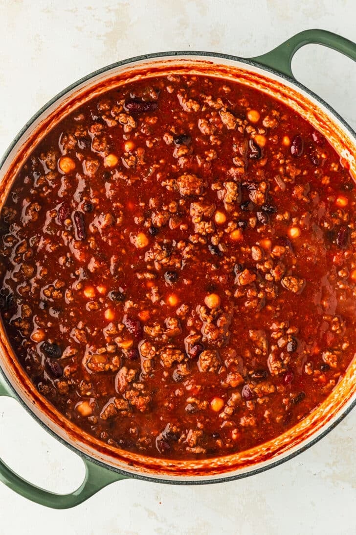 A green Dutch oven of chili for a chili toppings charcuterie board.