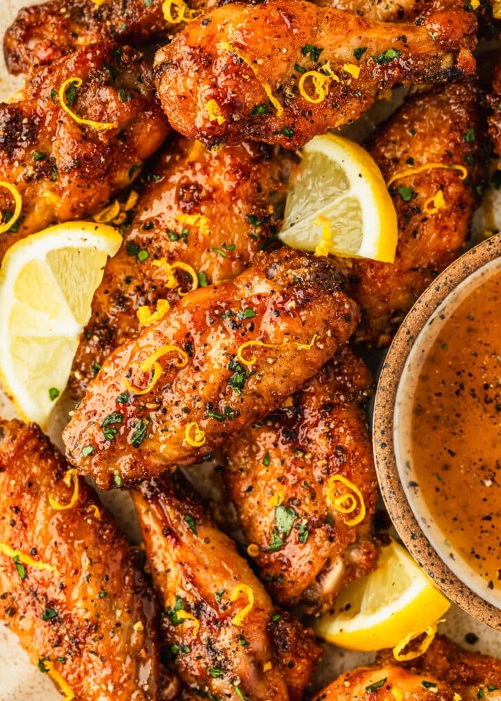 Lemon pepper honey wings topped with lemon slices, next to a white bowl of sauce.