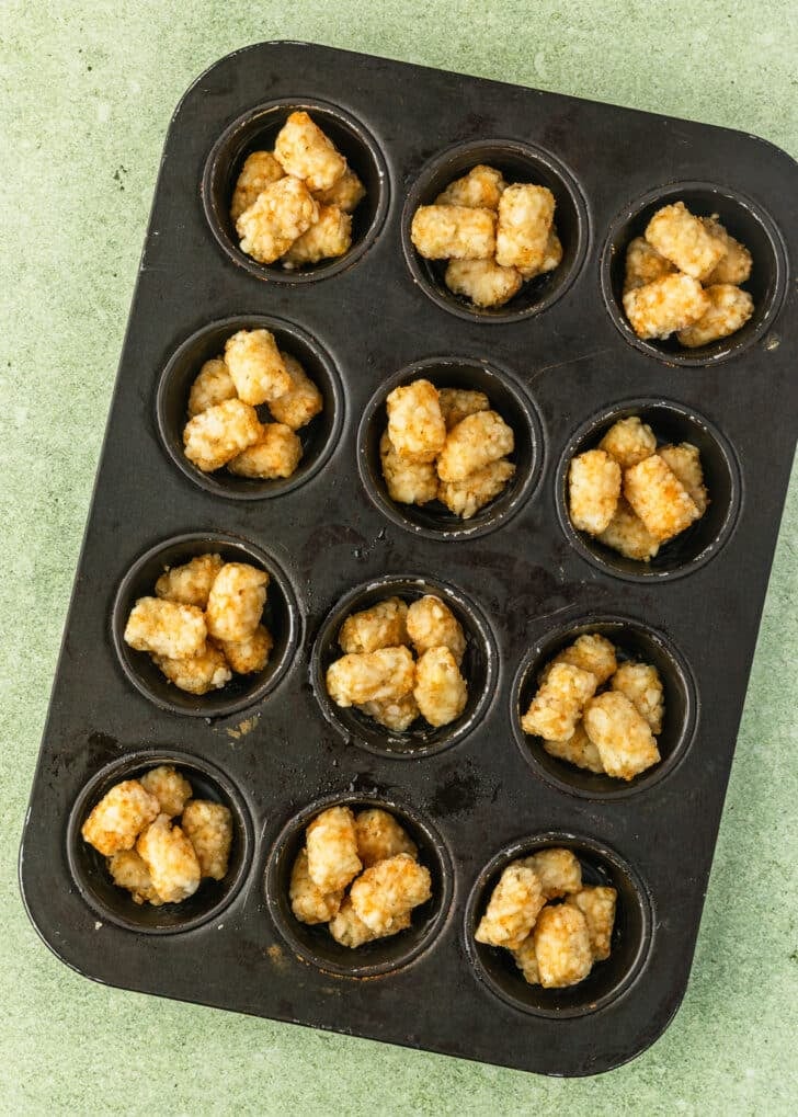 A cupcake pan of tater tots on a green counter.