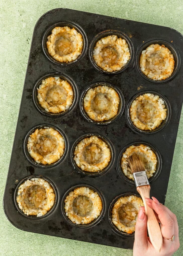 A hand using a pastry brush to brush tater tot bites with butter.
