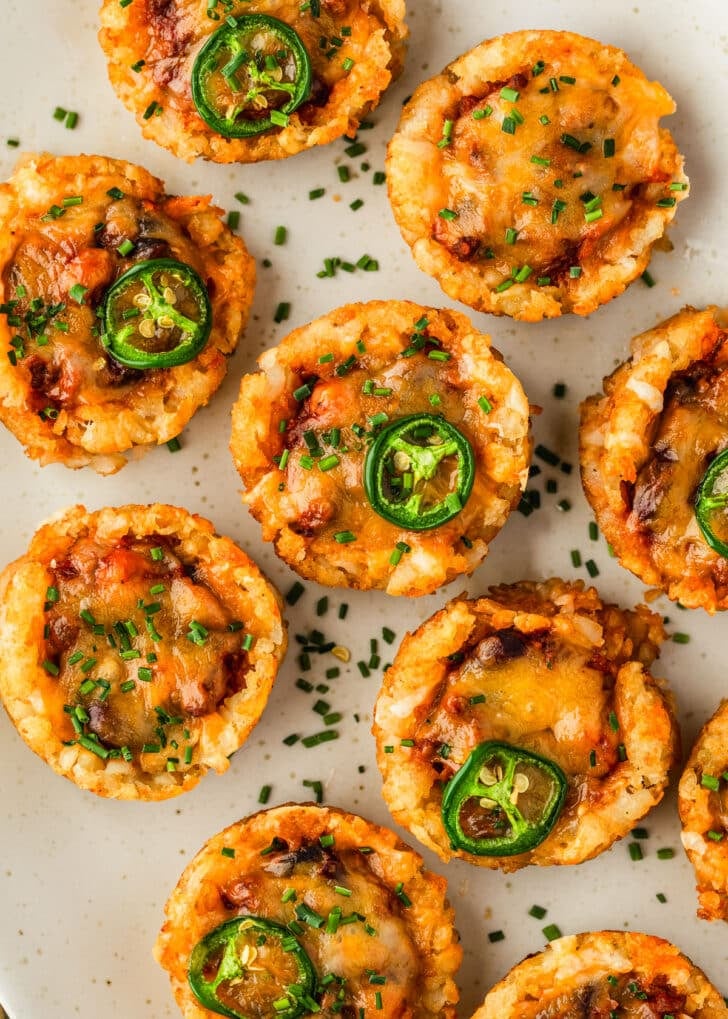 A white platter of tater tot chili cheese cups with jalapenos.